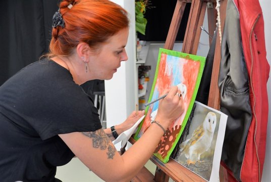 Bei der Vernissage führt Alexandra Keller live eine Airbrush-Arbeit vor. Nach dem Aufsprühen wird die Farbe partiell wieder entfernt, um anschließend mit Künstlerbuntstiften Akzente zu setzen. (Foto: © Martina Hörle)