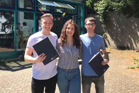 Die beiden Azubis Jonas Rüttgers (li.) und André Lucas gemeinsam mit AWEOS-Grafikdesignerin Carina Laport bei der Abschlussfeier vor dem TBK Solingen. (Foto: © AWEOS)