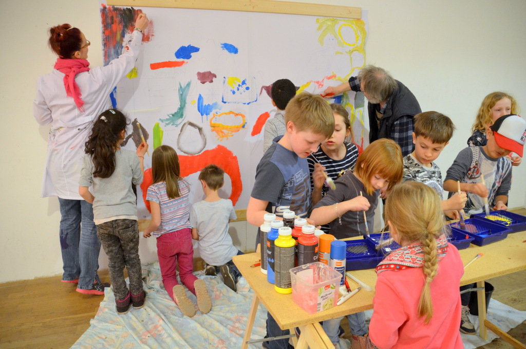 Gemeinsam mit den Künstlern Saskia Bela und Lothar Ruthmann gestalteten die Kinder der Grundschule Schützenstraße ein fröhliches und buntes Gemeinschaftswerk, das in Kürze auf dem Ferien(s)pass-Plakat zu sehen sein wird. (Foto: © Martina Hörle)
