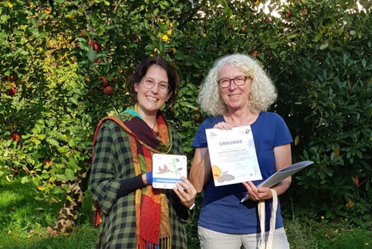 Annette Kalde (re.) vom NABU überreicht die Urkunde für den schmetterlingsfreundlichen Garten an Hobbygärtnerin Sarah Schmitz. (Foto: © Christoph Kalde)