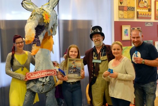 Die zehnjährige Celine hatte bei der Namensfindung gewonnen. Am Samstag nahm sie in Begleitung ihrer Eltern von Künstler Lothar Ruthmann (Mitte) ihren Preis, ein gerahmtes Bild des „Waschlappens“, entgegen. Saskia Bela (li.) hatte die Karte aus der Lostrommel gezogen. (Foto: © Martina Hörle)