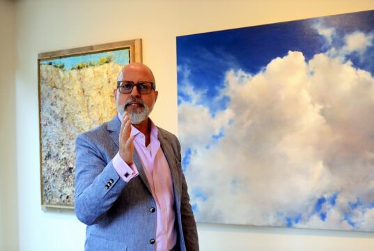 Frank Schablewski, Schriftsteller und Installationskünstler, führt am kommenden Samstag virtuell durch die Ausstellung „Vier Elemente“. Hier steht er vor dem fast fotorealistischen Wolkenbild des Künstlers Gunnar Wolf (Foto: © Martina Hörle)