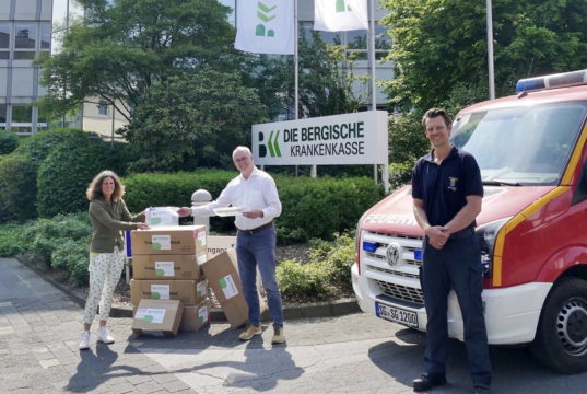 Sabine Stamm, Vorständin der Bergischen Krankenkasse, übergibt die Schutzausrüstung an Roland Blank (mi.), Einkaufsleiter der Solinger Stadtverwaltung, und Daniel Karschges von der Feuerwehr. (Foto: © Stephanie Schmidt/BKK)