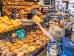 Evertzberg-Mitarbeiterin Dajana Murati übergibt Erstklässler David eine gefüllte, gelbe Snackbox. (Foto: © Thomas Wunsch)