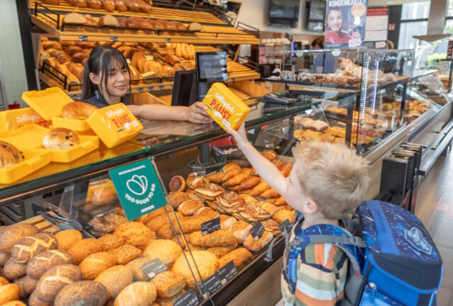 Evertzberg-Mitarbeiterin Dajana Murati übergibt Erstklässler David eine gefüllte, gelbe Snackbox. (Foto: © Thomas Wunsch)