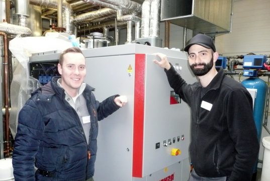 „Läuft“, Patrick Preiss (li.), Energiemanager der Technischen Abteilung der Kplus Gruppe, und Kemal Hilmi Dogan, Technischer Betriebsleiter der Genesis Zentralküche, freuen sich über die Installation des neuen Blockheizkraftwerks an der Alsenstraße. (Foto: © Kplus Gruppe)