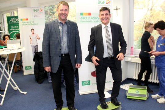 Gregor Hellmons (links), Sprecher der Geschäftsführung der Kplus Gruppe, und Oliver Hartmann (rechts), Regionaldirektor der AOK, versuchen sich auf dem Bewegungsparcour im Kplus Forum Solingen. (Foto: © Bastian Glumm)