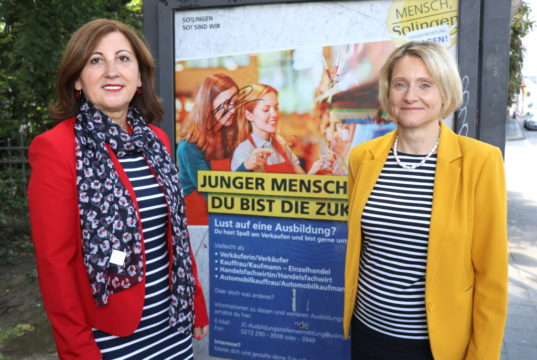 Maria Ricchiuti (li.) und Kristin Degener vom Kommunalen Jobcenter vor einem City-Light-Poster der Kampagne. Die Poster sind seit Dienstag an Bushaltestellen im Stadtgebiet angebracht. (Foto: © Bastian Glumm)