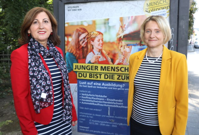 Maria Ricchiuti (li.) und Kristin Degener vom Kommunalen Jobcenter vor einem City-Light-Poster der Kampagne. Die Poster sind seit Dienstag an Bushaltestellen im Stadtgebiet angebracht. (Foto: © Bastian Glumm)