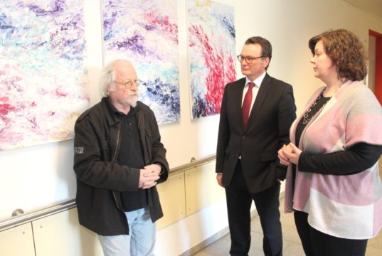15 farbenfrohe Bilder schenkte Künstler Ernst Theis (li.) dem Klinikum. Die Geschäftsführung des Hauses, Barbara Matthies und Prof. Dr. Thomas Standl, ist dafür sehr dankbar. (Foto: © Bastian Glumm)