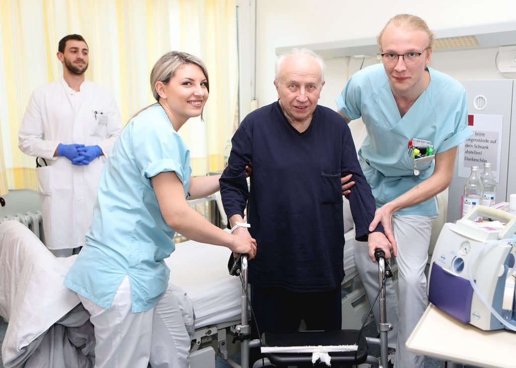 Hermine Harder (li.) und Philipp Röltgen (re.) helfen einem Patienten der St. Lukas Klinik. Im Hintergrund Assistenzarzt Tariq Al-Hindi. (Foto: © Kplus Gruppe)