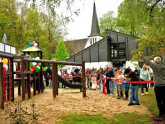 Kinder durchschneiden das rote Band zur Eröffnung des neuen Spielplatz hinter dem Aufderhöher Gemeindezentrum, zahlreiche Besucher verfolgen den offiziellen Start. (Foto: © Petra Schelkes)