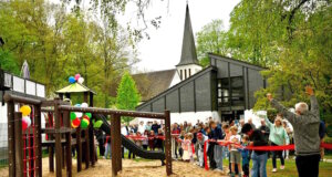 Kinder durchschneiden das rote Band zur Eröffnung des neuen Spielplatz hinter dem Aufderhöher Gemeindezentrum, zahlreiche Besucher verfolgen den offiziellen Start. (Foto: © Petra Schelkes)