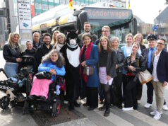 Teilnehmer und Projektbeteiligte bei der Auftaktfahrt der neuen O-Bus-Quiztour am Graf-Wilhelm-Platz: mit dabei Kater Salabim (im Kostüm: Sandra Kratz), Schirmherrin Sonja Flemm (li. daneben), Bürgermeisterin Ioanna Zacharaki (re. neben dem Kater) sowie Sandra-Janine Schneider (7. v. rechts) vor dem Sonderwagen der Linie 681. (Foto: © Bastian Glumm)