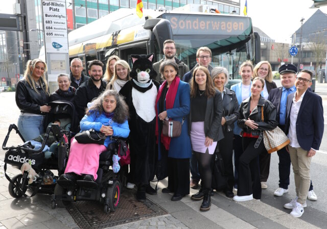 wegfinder-quiztour-salabim-obus (1) Teilnehmer und Projektbeteiligte bei der Auftaktfahrt der neuen O-Bus-Quiztour am Graf-Wilhelm-Platz: mit dabei Kater Salabim (im Kostüm: Sandra Kratz), Schirmherrin Sonja Flemm (li. daneben), Bürgermeisterin Ioanna Zacharaki (re. neben dem Kater) sowie Sandra-Janine Schneider (7. v. rechts) vor dem Sonderwagen der Linie 681. (Foto: © Bastian Glumm)